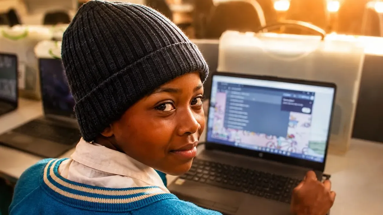 A young learner smiling at the camera while using a laptop at the Northam ICT Centre