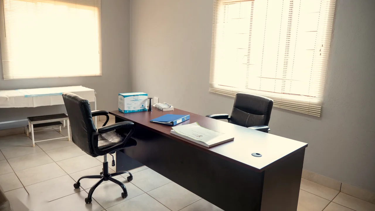 A consulting room with desk, chairs and an examination bed